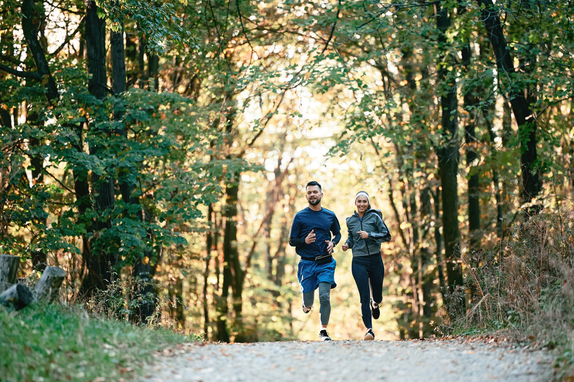 a man and woman running on a trail in the woods