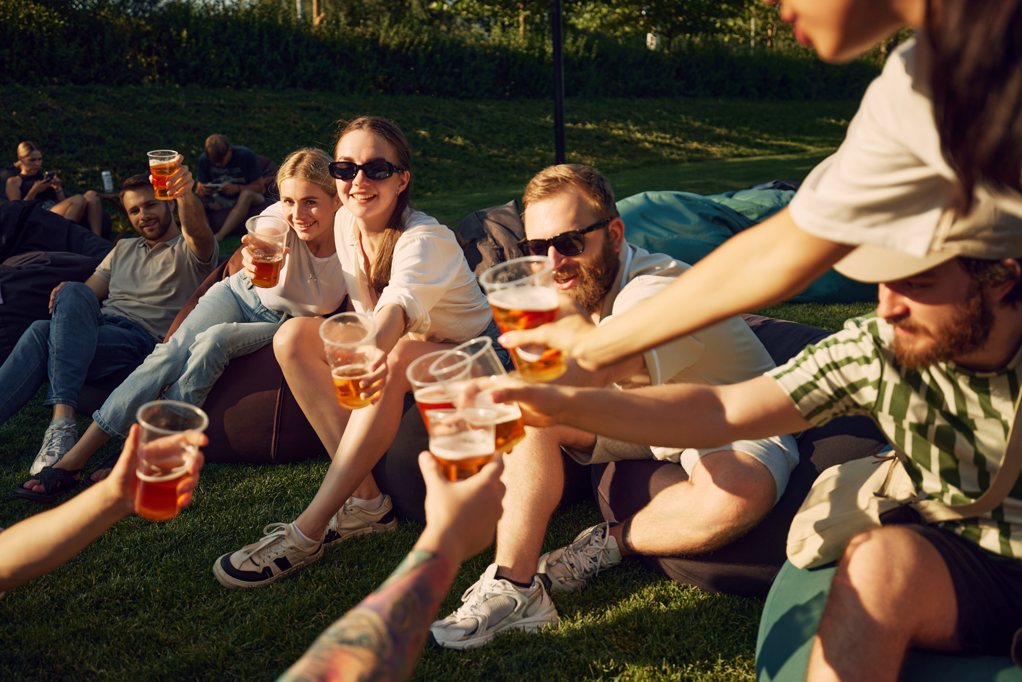a group of people sitting on the grass holding drinks